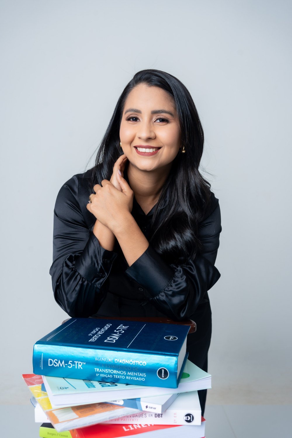 Luiza Yandara, psicóloga clínica CRP 05/86037, sorrindo apoiada em uma pilha de livros de psicologia